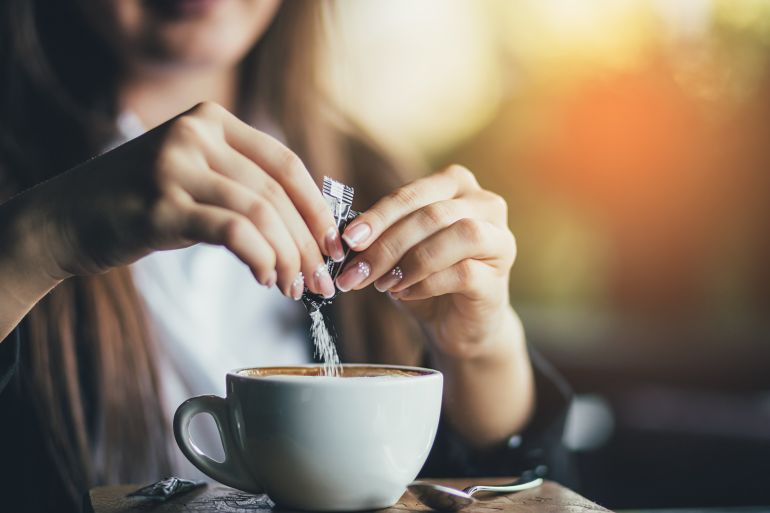 Female hand pours sugar into coffee. Sunlight background