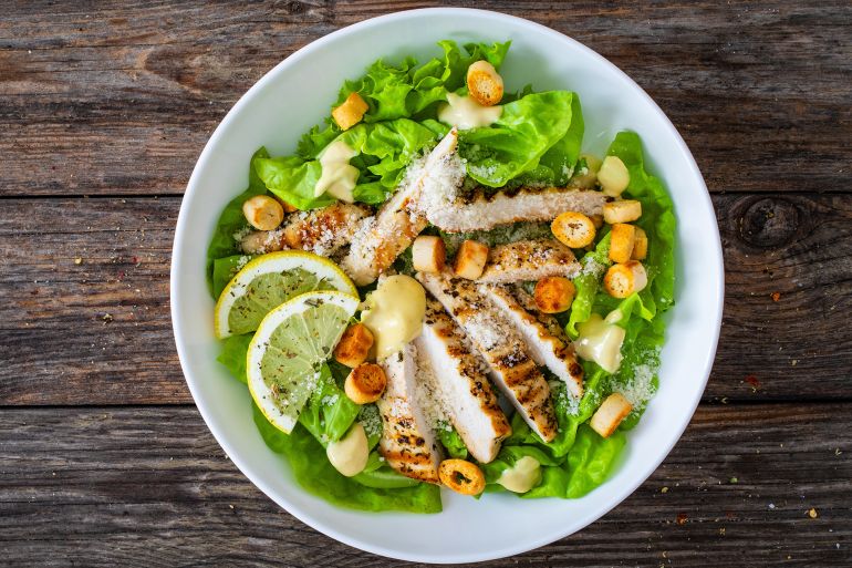 Caesar salad - fried chicken breast and vegetables on wooden table ; Shutterstock ID 2329230995; purchase_order: AJA; job: ; client: ; other: