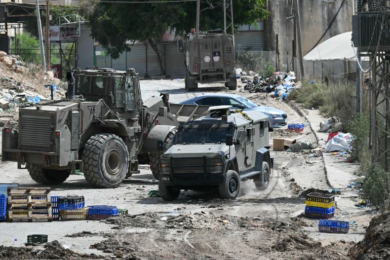 Israeli military armoured vehicles including a bulldozer block a road during a raid in the al-Faraa camp for Palestinian refugees near Tubas city in the occupied West Bank on August 28, 2024. - The Israeli army targeted four cities as it launched a major operation in the occupied West Bank on August 28, with the Palestinian Red Crescent reporting at least 10 dead. (Photo by RONALDO SCHEMIDT / AFP)