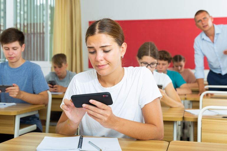 Interested girl high school student using mobile phone to find necessary information on lecture in class. Concept of using technology in education