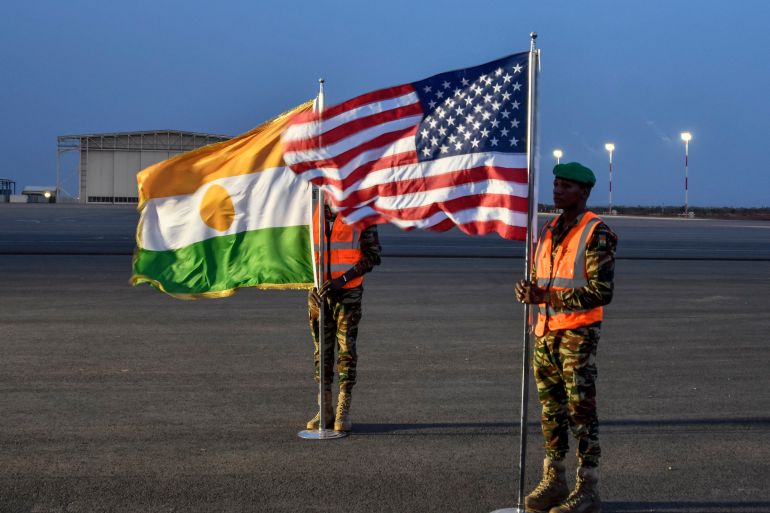 Two Nigerien soldiers hold the American and Nigerien flags on Air Base 101 in Niamey on June 7, 2024 during the ceremony for the first departure of American troops from Niger. (Photo by BOUREIMA HAMA / AFP)