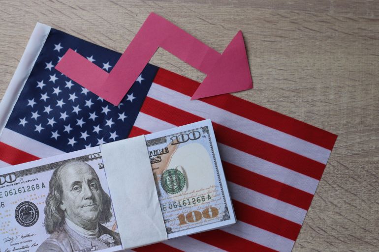 Red arrow going down on a background of money and US flag. The concept of changing course of US dollar on ...