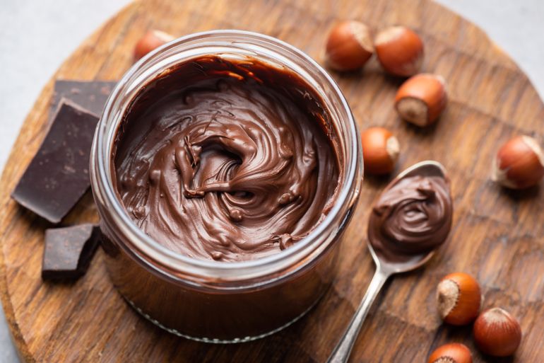 Hazelnut chocolate spread in a jar on wooden board, closeup view. Sweet chocolate cream spread or butter