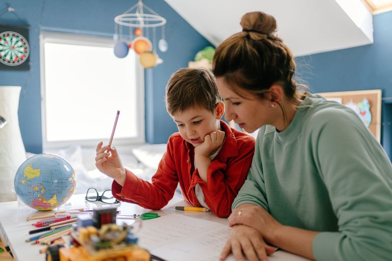 Photo of a young boy being homeschooled by his mother in his bedroom